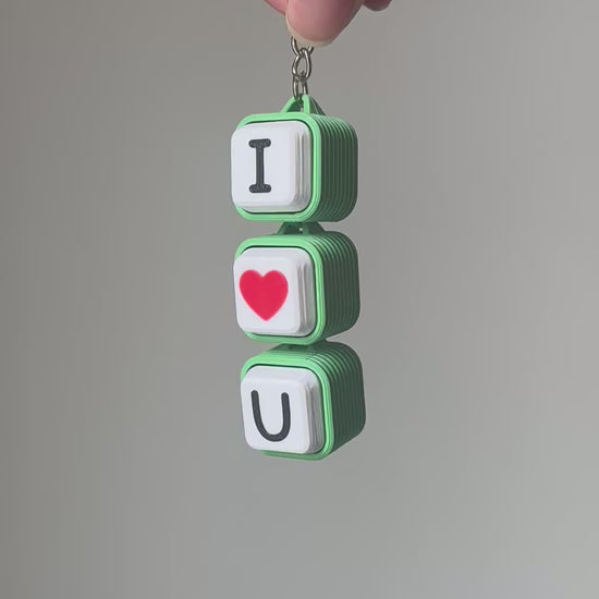 Demonstration video of a green and white 'I Love U' 3D-printed keychain. A hand presses each keycap in order—'I', red heart, 'U'—producing crisp mechanical clicking sounds.