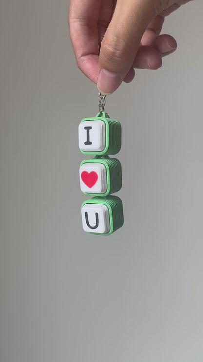 Demonstration video of a green and white 'I Love U' 3D-printed keychain. A hand presses each keycap in order—'I', red heart, 'U'—producing crisp mechanical clicking sounds.