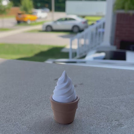 Video of a hand pressing down on a 3D-printed vanilla soft-serve ice cream fidget clicker, demonstrating its crisp clicking action and smooth white swirl top set in a brown cone.
