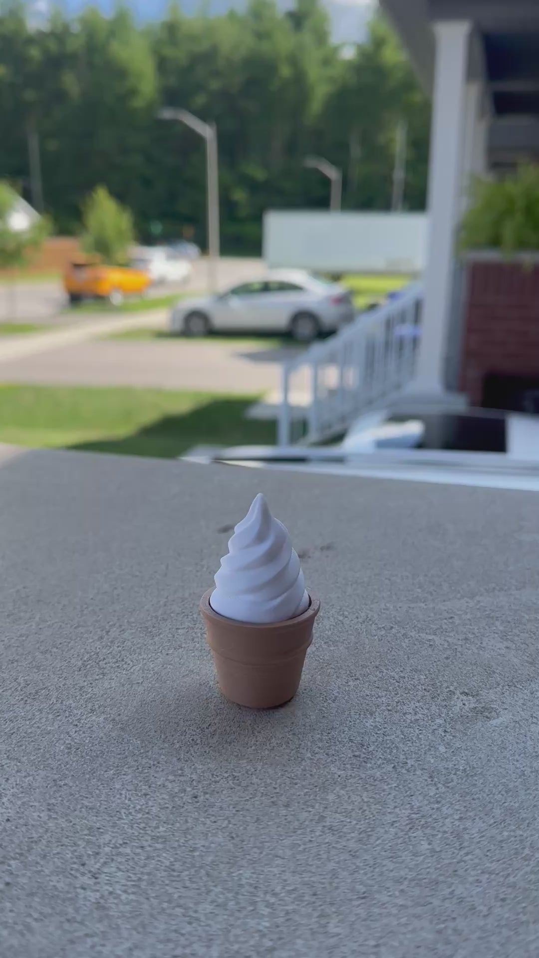 Video of a hand pressing down on a 3D-printed vanilla soft-serve ice cream fidget clicker, demonstrating its crisp clicking action and smooth white swirl top set in a brown cone.
